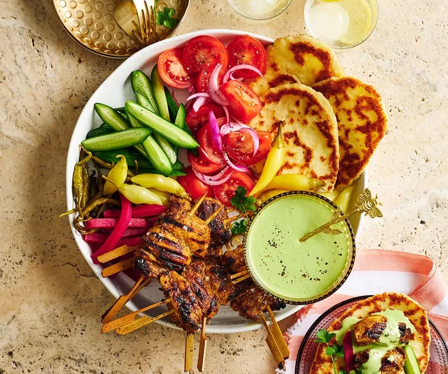 Sliced chicken shawarma on a platter with fresh herbs, pita bread, and colorful vegetables arranged around it