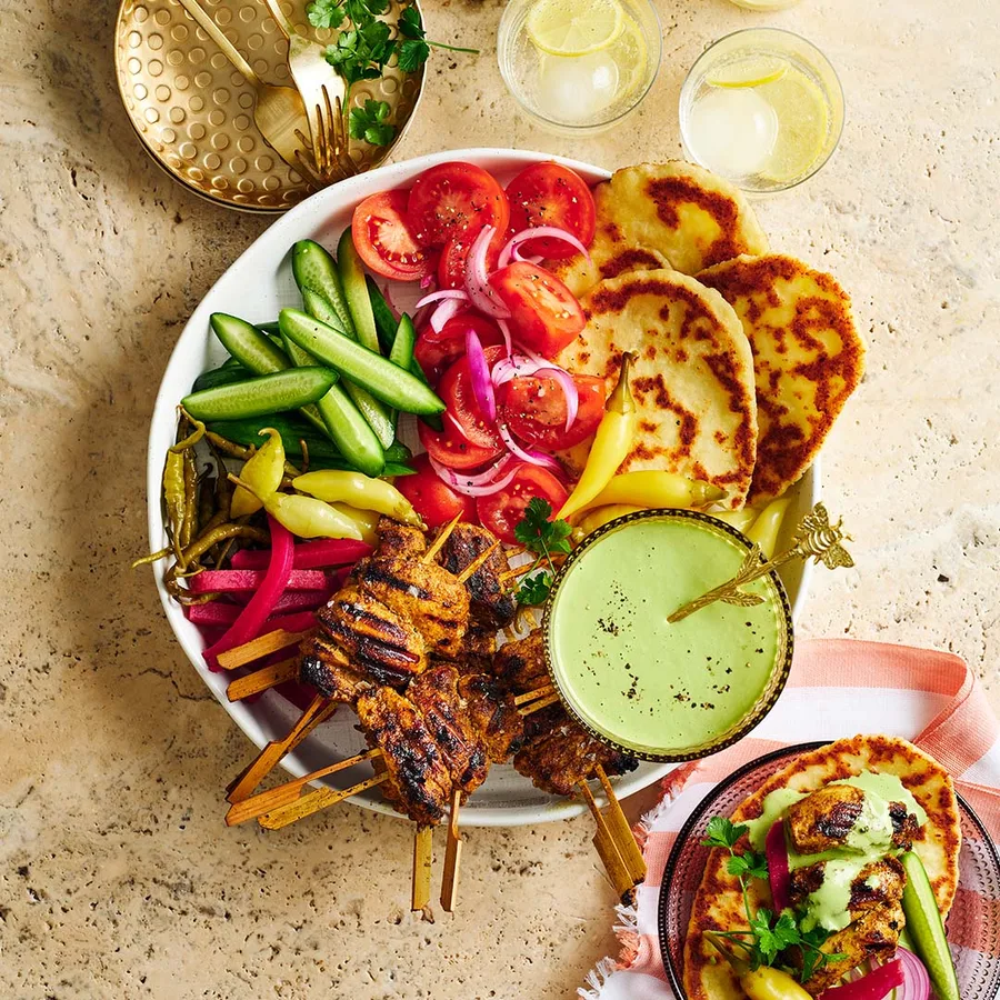 Sliced chicken shawarma on a platter with fresh herbs, pita bread, and colorful vegetables arranged around it