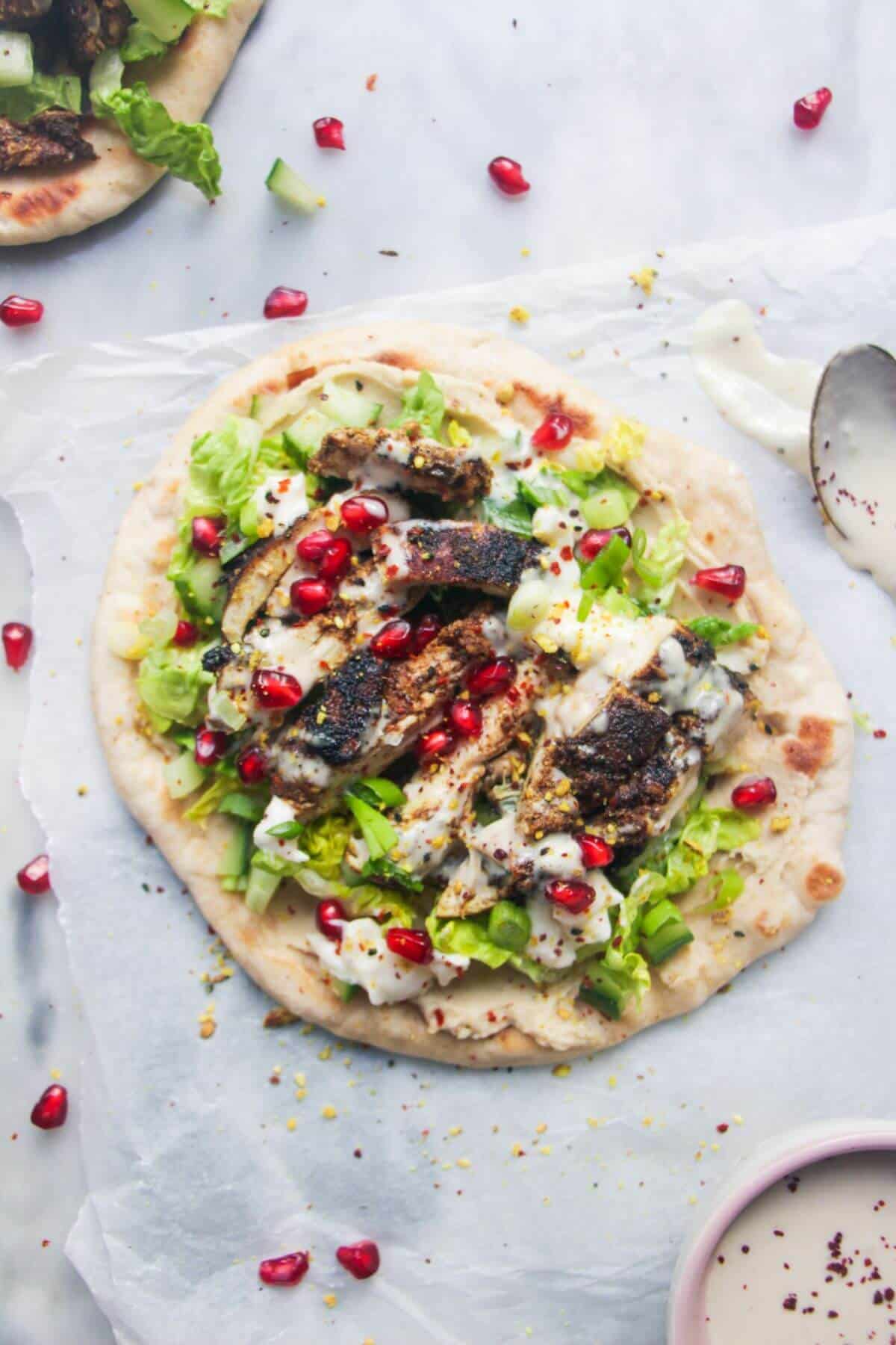 Close-up shot of chicken shawarma wrapped in warm pita bread with fresh cucumbers, tomatoes, and creamy tahini sauce drizzling down