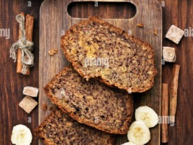 Golden brown banana bread loaf sliced on a wooden cutting board with butter and a knife nearby, natural lighting showing the moist, tender crumb