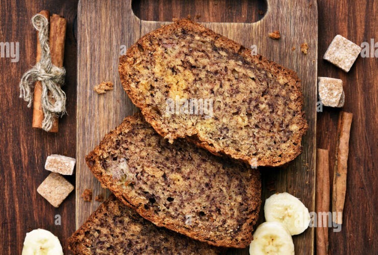 Golden brown banana bread loaf sliced on a wooden cutting board with butter and a knife nearby, natural lighting showing the moist, tender crumb