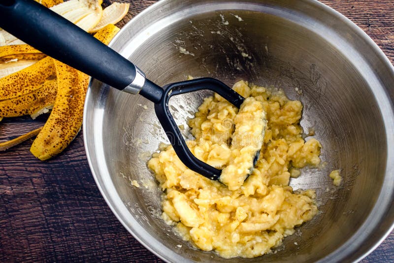 Mixing bowl with mashed bananas and wet ingredients being combined, showing the lumpy texture before flour is added