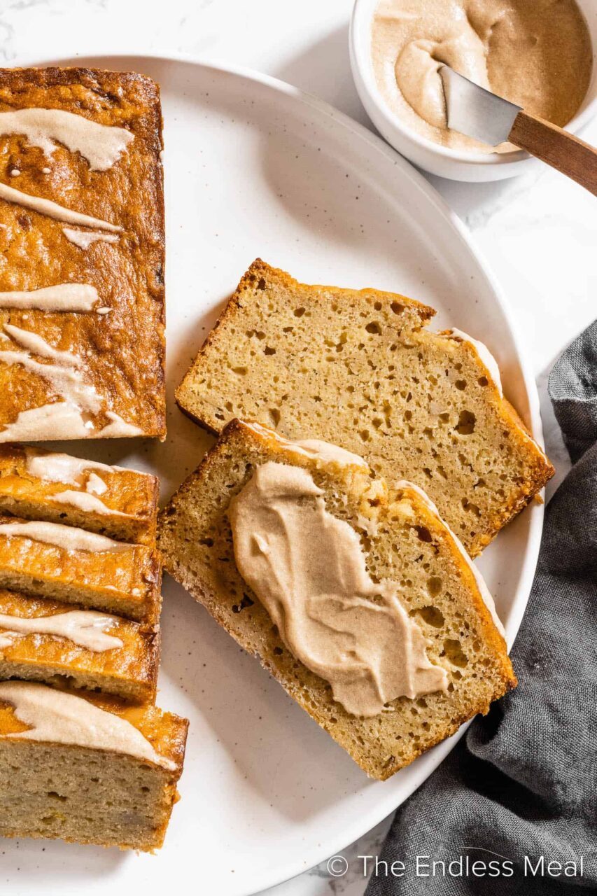 Close-up slice of banana bread on a white plate with a pat of melting butter, showing the moist, tender crumb texture