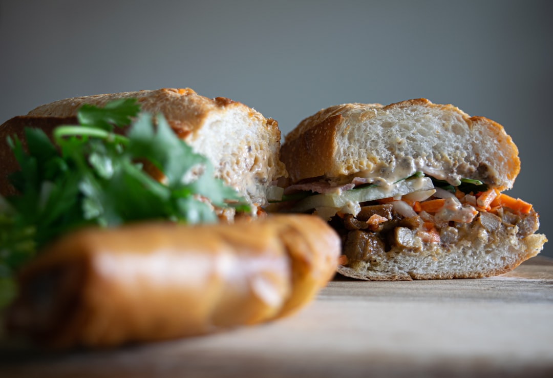 Close-up cross-section shot of a banh mi sandwich showing layers of pickled vegetables, herbs, protein, and crispy bread texture