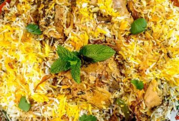 Overhead shot of chicken biryani in a large pot with golden rice, tender chicken pieces, and fresh herbs garnish