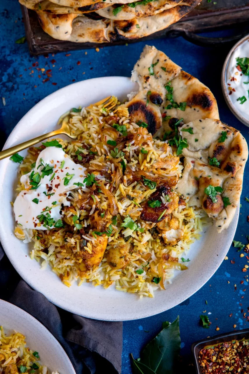 Close-up shot of a serving bowl filled with chicken biryani, showing the layered rice and chicken with a garnish of fresh cilantro and sliced almonds