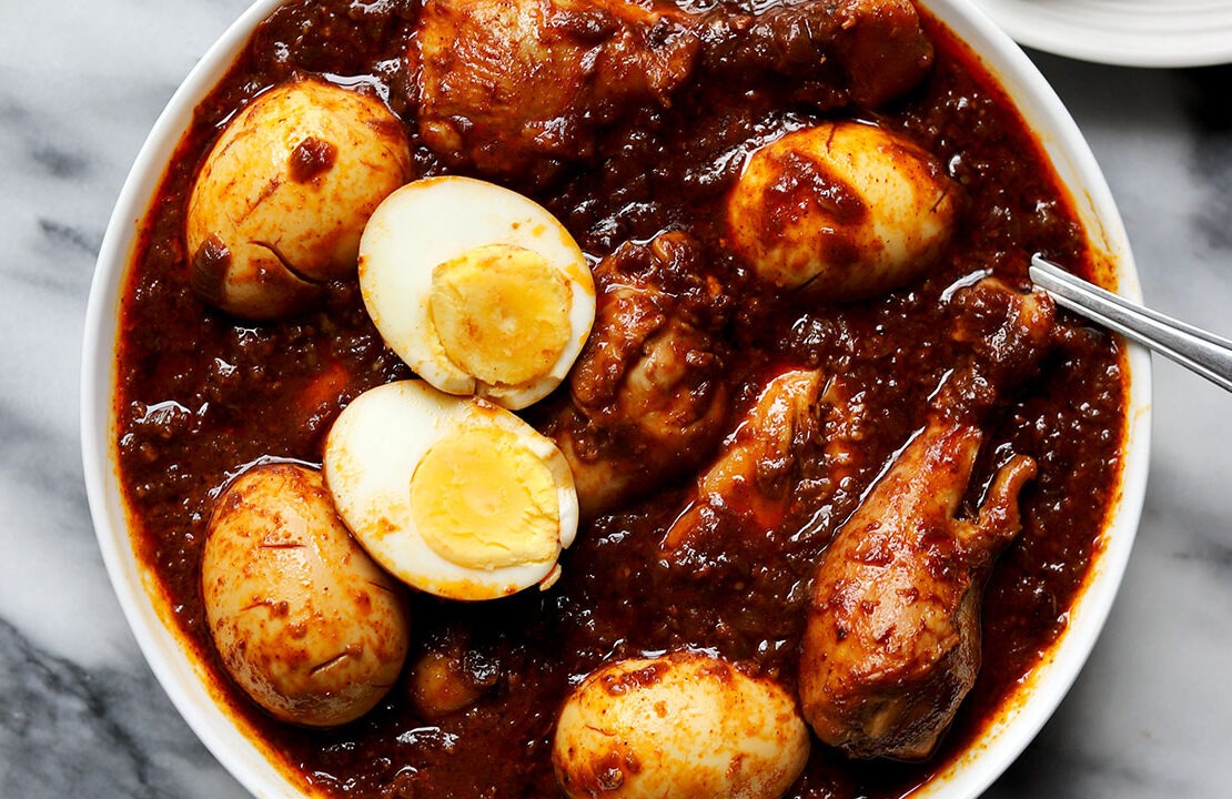 Ethiopian Doro Wat served in a traditional clay pot with hard-boiled eggs visible, garnished with fresh herbs, with injera bread on the side