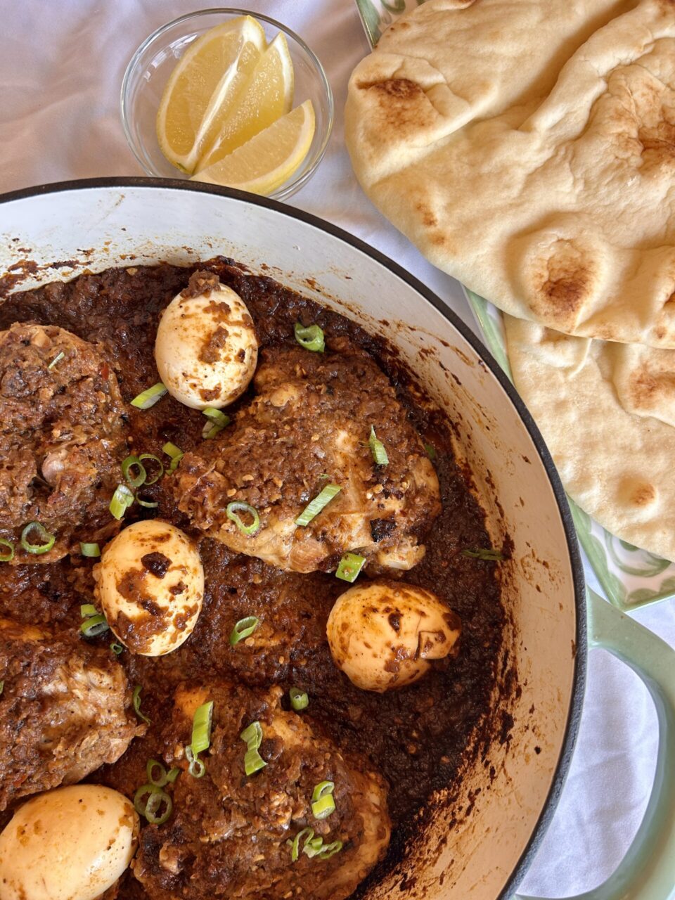 Close-up of a spoon lifting tender chicken and egg from the rich, dark red Doro Wat sauce, showing the glossy, well-developed texture