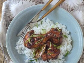 Filipino chicken adobo in a large skillet with glossy dark sauce, garnished with green onions, served alongside steamed white rice