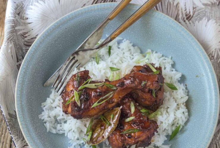 Filipino chicken adobo in a large skillet with glossy dark sauce, garnished with green onions, served alongside steamed white rice