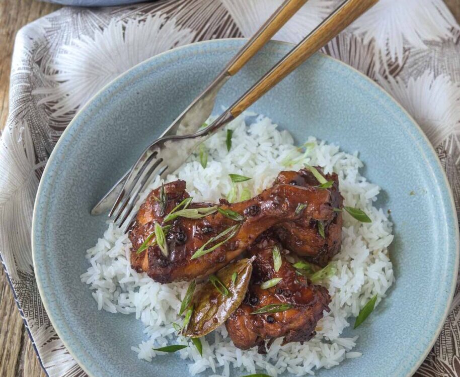 Filipino chicken adobo in a large skillet with glossy dark sauce, garnished with green onions, served alongside steamed white rice