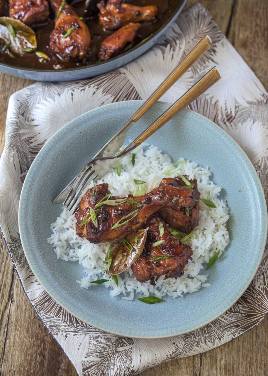 Filipino chicken adobo in a large skillet with glossy dark sauce, garnished with green onions, served alongside steamed white rice