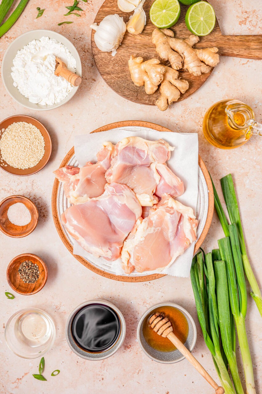 Raw chicken thighs in a bowl with soy sauce, vinegar, and garlic cloves arranged nearby on a wooden cutting board