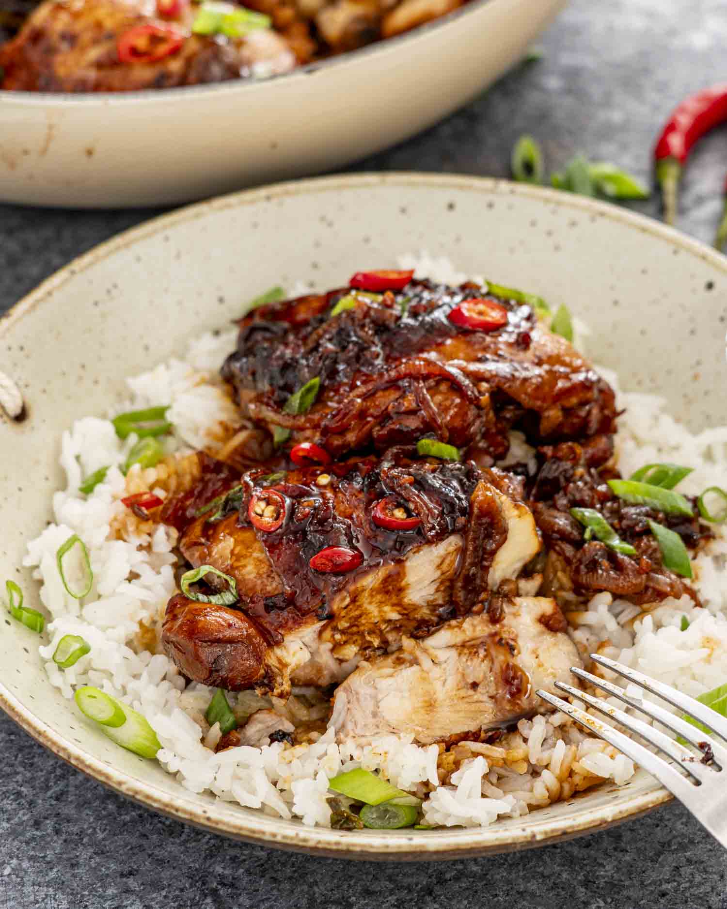 Close-up shot of tender chicken adobo over steamed rice with sauce pooling around it, garnished with sliced green onions and a bay leaf