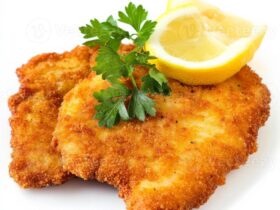Golden crispy German schnitzel cutlets on a white plate with lemon wedges and parsley garnish