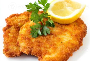 Golden crispy German schnitzel cutlets on a white plate with lemon wedges and parsley garnish