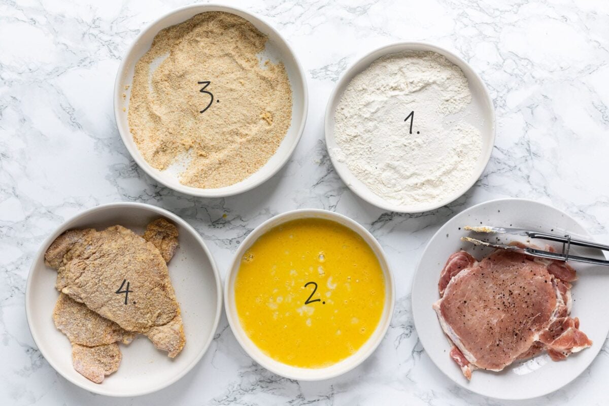 Three shallow dishes showing the breading station setup with flour, beaten eggs, and breadcrumbs