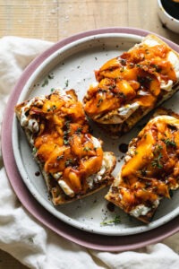 Grilled peach burrata breakfast toast on rustic wooden board with golden caramelized peaches and torn creamy burrata on thick whole grain bread slices