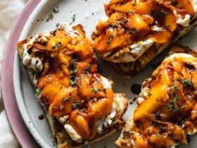 Grilled peach burrata breakfast toast on rustic wooden board with golden caramelized peaches and torn creamy burrata on thick whole grain bread slices