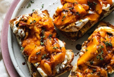 Grilled peach burrata breakfast toast on rustic wooden board with golden caramelized peaches and torn creamy burrata on thick whole grain bread slices