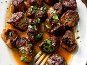 Crispy golden Haitian griot pork cubes served on a white platter with rice and beans, garnished with fresh herbs and lime wedges
