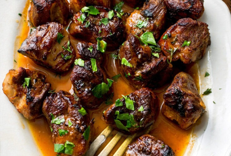Crispy golden Haitian griot pork cubes served on a white platter with rice and beans, garnished with fresh herbs and lime wedges