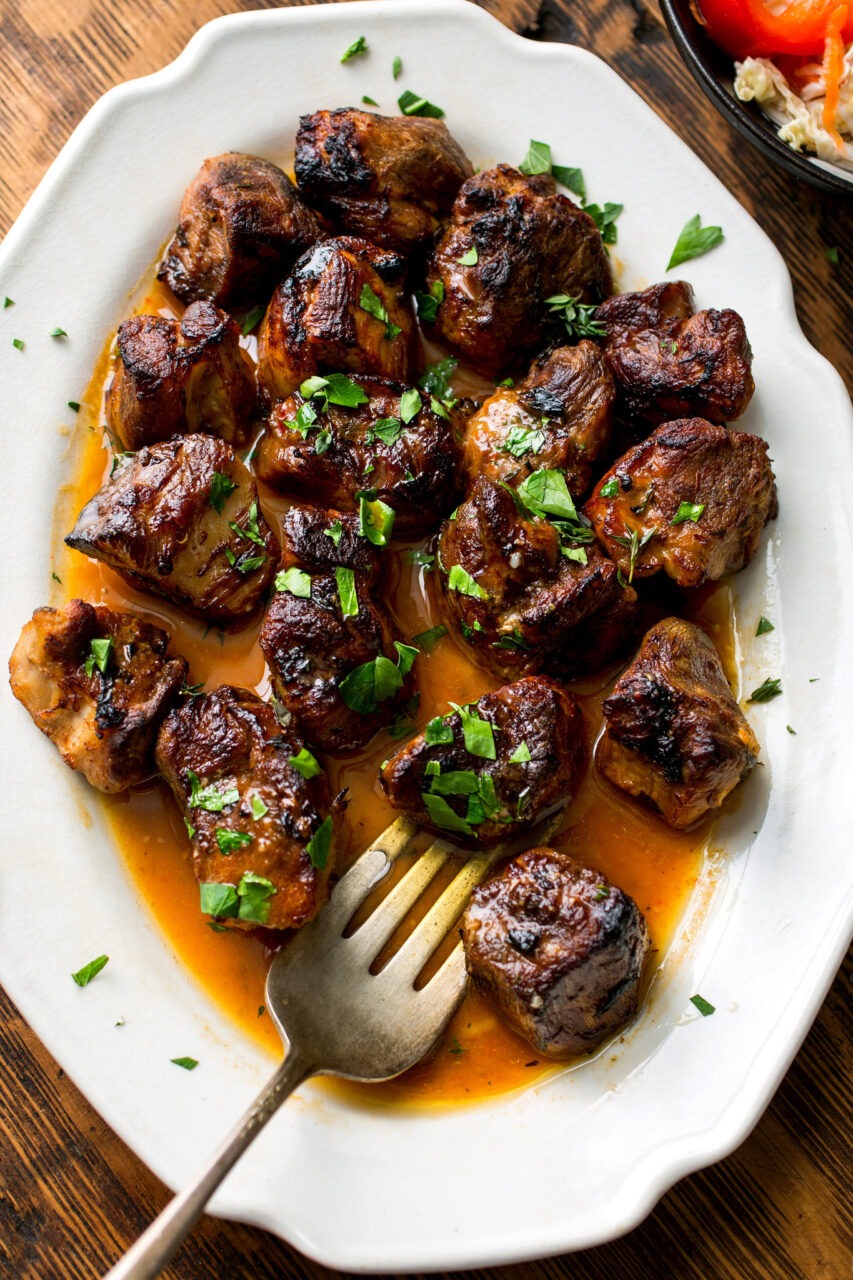 Crispy golden Haitian griot pork cubes served on a white platter with rice and beans, garnished with fresh herbs and lime wedges