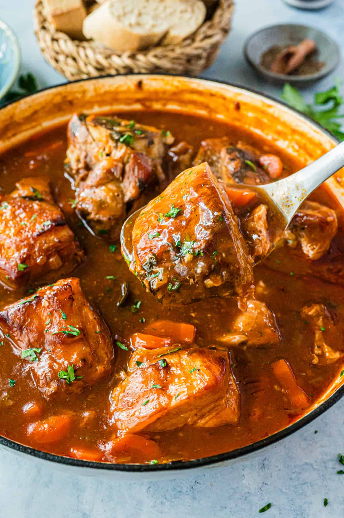 Raw seasoned pork shoulder cubes in a large pot with garlic, herbs and citrus, ready for braising
