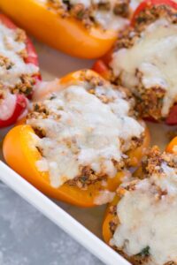 Colorful stuffed bell pepper boats filled with ground turkey quinoa and Mediterranean herbs on a white serving platter, garnished with fresh parsley and crumbled feta