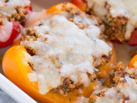 Colorful stuffed bell pepper boats filled with ground turkey quinoa and Mediterranean herbs on a white serving platter, garnished with fresh parsley and crumbled feta