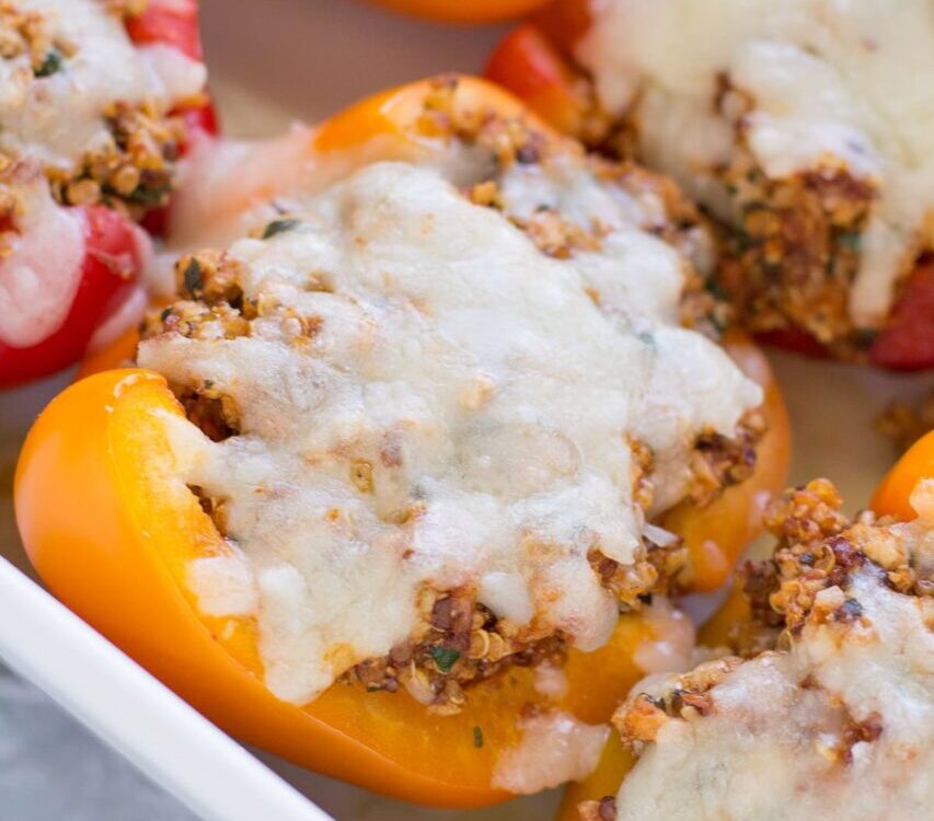 Colorful stuffed bell pepper boats filled with ground turkey quinoa and Mediterranean herbs on a white serving platter, garnished with fresh parsley and crumbled feta