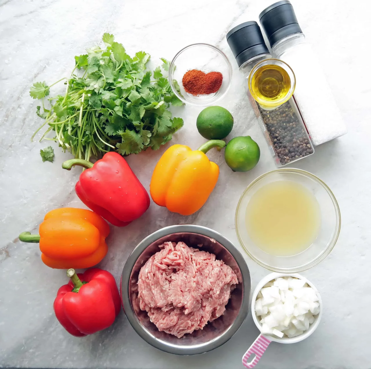 Overhead flat-lay of halved bell peppers, ground turkey in a skillet, cooked quinoa in a bowl, and Mediterranean herbs and spices on a wooden cutting board