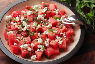 Colorful watermelon feta mint salad in a white serving bowl with fresh mint garnish on a rustic wooden table