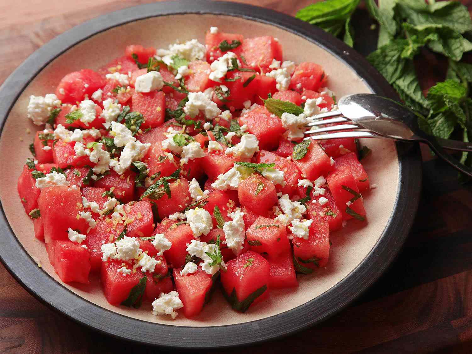 Colorful watermelon feta mint salad in a white serving bowl with fresh mint garnish on a rustic wooden table