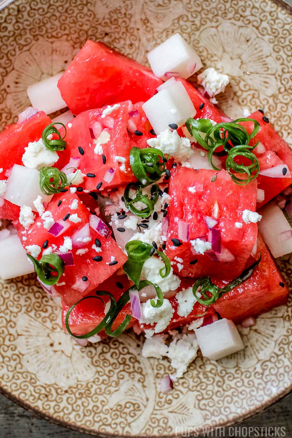 Close-up shot of watermelon feta salad in a glass meal prep container with a fork, showing the fresh mint and glistening watermelon cubes