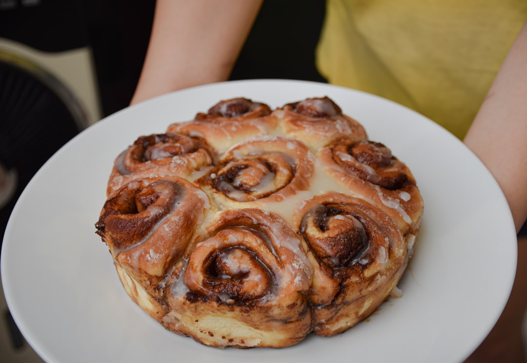 Close-up shot of a single cinnamon roll being pulled apart, showing the gooey cinnamon filling and soft, fluffy texture with glaze dripping down the sides