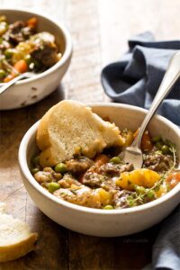 Instant Pot beef stew served in rustic ceramic bowls with fresh herbs and crusty bread, showing tender beef and colorful vegetables in rich broth