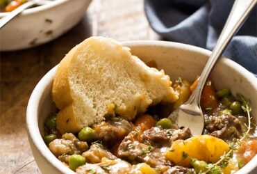 Instant Pot beef stew served in rustic ceramic bowls with fresh herbs and crusty bread, showing tender beef and colorful vegetables in rich broth