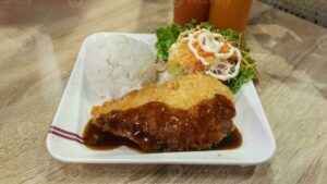 Golden crispy Japanese chicken katsu cutlets served on a white plate with shredded cabbage, steamed rice, and katsu sauce drizzled on top