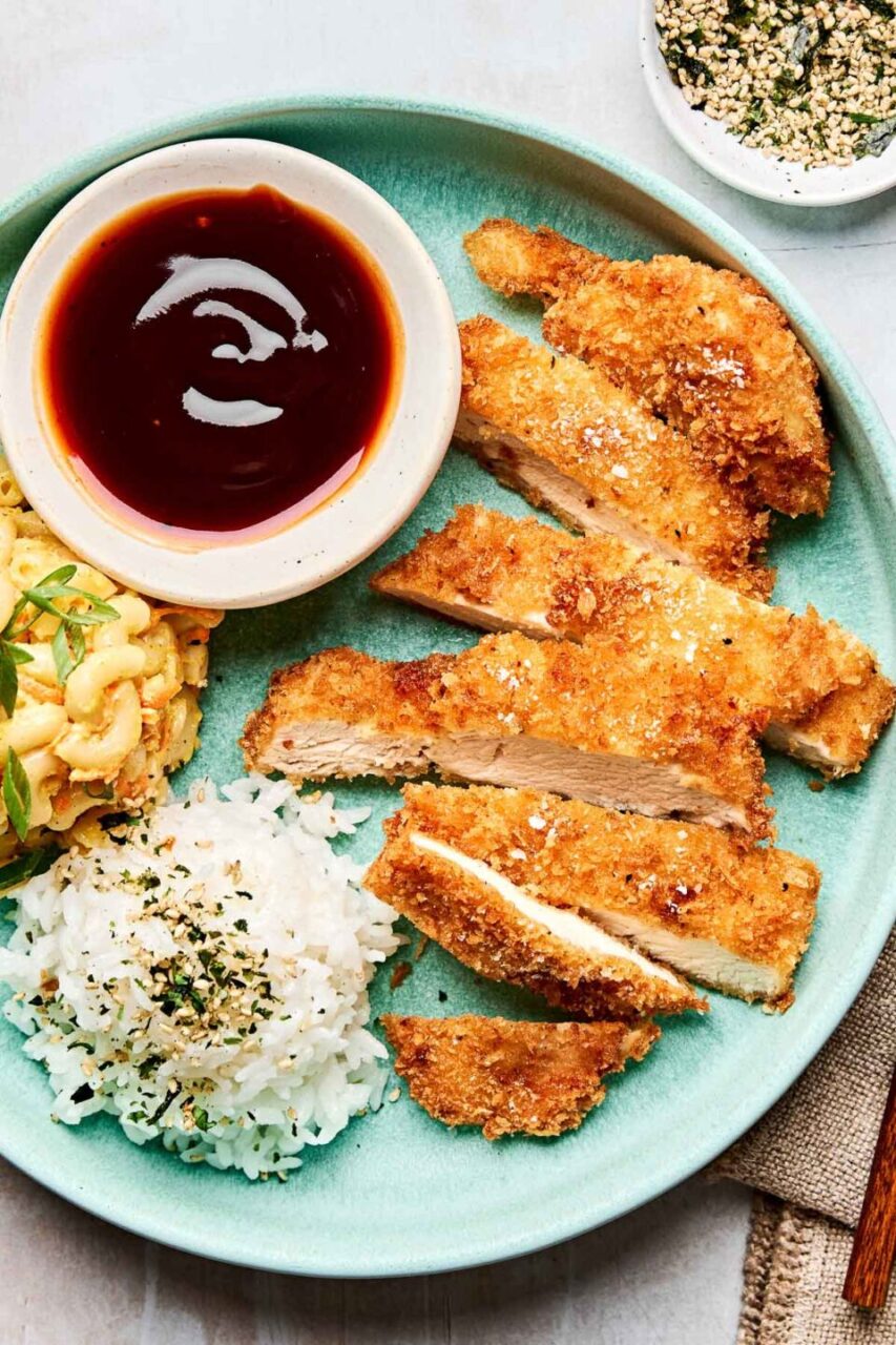 Close-up shot of sliced Japanese chicken katsu showing the golden crispy exterior and juicy white meat interior, served with a small bowl of katsu sauce for dipping