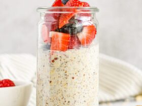 Overnight oats with summer berries in a glass mason jar, layered with Greek yogurt, strawberries, blueberries, and raspberries, topped with honey drizzle, photographed on a bright white marble surface with fresh mint garnish
