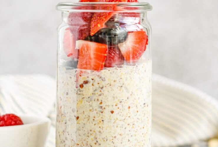 Overnight oats with summer berries in a glass mason jar, layered with Greek yogurt, strawberries, blueberries, and raspberries, topped with honey drizzle, photographed on a bright white marble surface with fresh mint garnish