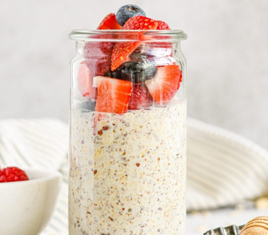 Overnight oats with summer berries in a glass mason jar, layered with Greek yogurt, strawberries, blueberries, and raspberries, topped with honey drizzle, photographed on a bright white marble surface with fresh mint garnish