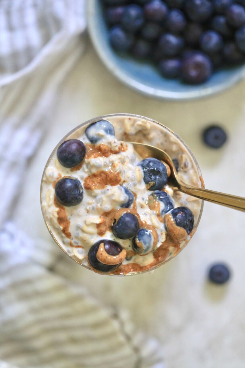 Close-up shot of a spoon lifting a creamy scoop of overnight oats with a fresh raspberry and blueberry balanced on top, shallow depth of field, warm morning light, soft bokeh background