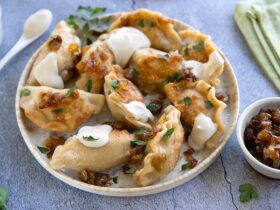 Golden pan-fried Polish pierogi on a rustic wooden plate, garnished with caramelized onions and fresh chives, with a dollop of sour cream on the side