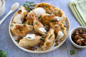 Golden pan-fried Polish pierogi on a rustic wooden plate, garnished with caramelized onions and fresh chives, with a dollop of sour cream on the side
