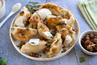 Golden pan-fried Polish pierogi on a rustic wooden plate, garnished with caramelized onions and fresh chives, with a dollop of sour cream on the side