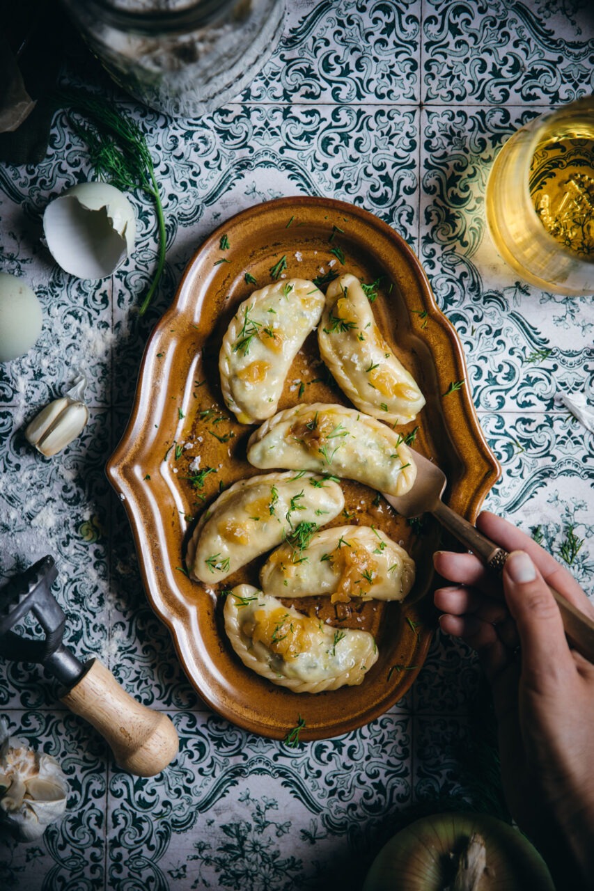 Close-up of a cut-open pierogi showing the creamy potato filling, served alongside caramelized onions and a garnish of fresh herbs