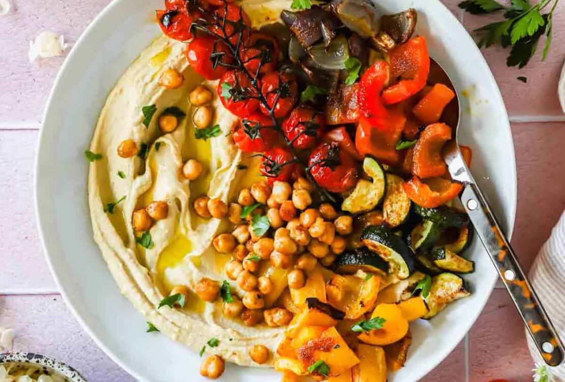 Roasted chickpea and vegetable hummus bowl beautifully plated with creamy hummus, crispy golden chickpeas, colorful fresh vegetables, and a drizzle of olive oil