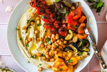 Roasted chickpea and vegetable hummus bowl beautifully plated with creamy hummus, crispy golden chickpeas, colorful fresh vegetables, and a drizzle of olive oil